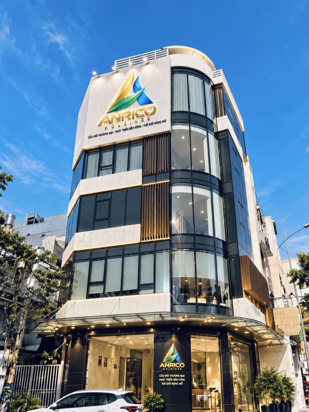 Tòa nhà trụ sở ANRICO HOLDINGS nhìn từ góc đường, mặt tiền kính và biển hiệu ANRICO HOLDINGS đặt trên tầng cao nhất